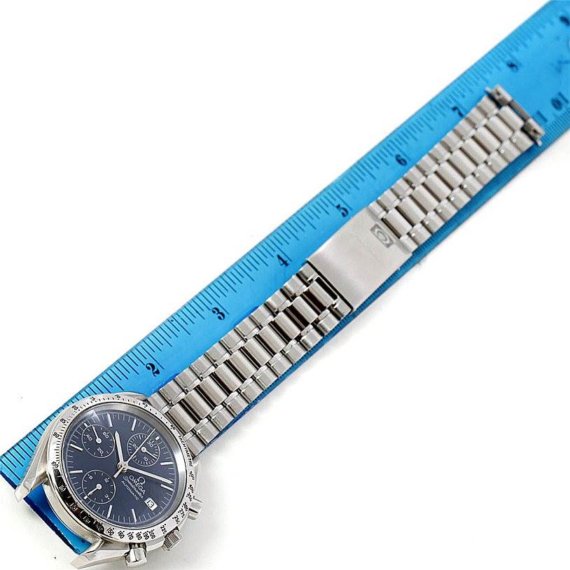 The image shows the front view of an Omega Speedmaster 3513.80.00 Men
s Stainless Steel Blue Dial 3513.80.00 Men
s Stainless Steel Blue Dial watch with its metal bracelet extended, measured against a blue ruler.