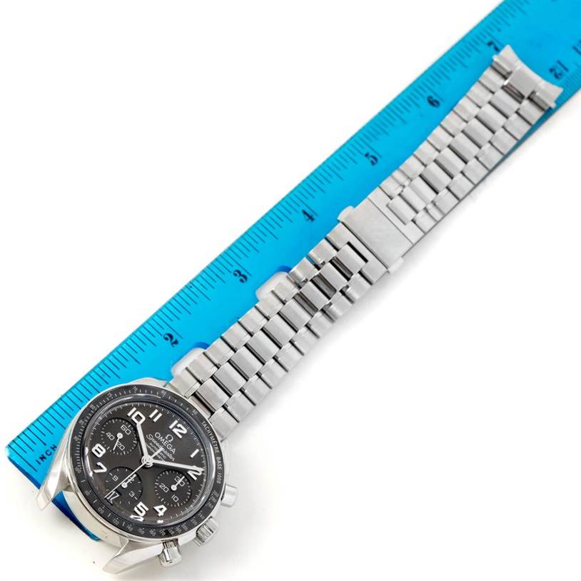 The image shows an Omega Speedmaster 324.30.38.40.06.001 Stainless Steel Grey Dial 324.30.38.40.06.001 Stainless Steel Grey Dial watch with its stainless steel bracelet laid next to a blue ruler for measurement.