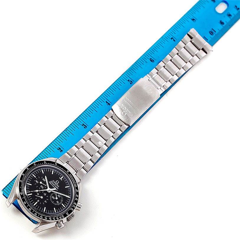 The Omega Speedmaster 48365704 Men
s Stainless Steel Black Dial 48365704 Men
s Stainless Steel Black Dial watch is shown from a top-down angle with a focus on the dial, bezel, and metal bracelet against a blue ruler.