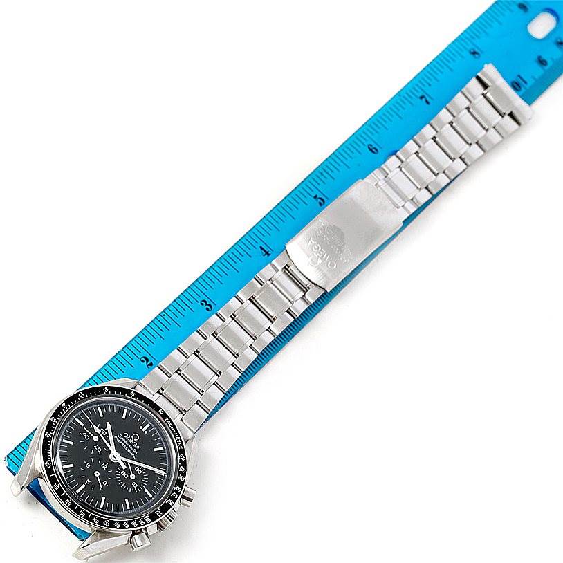 The image shows an Omega Speedmaster 3560.50.00 Men
s Stainless Steel Black Dial 3560.50.00 Men
s Stainless Steel Black Dial watch laid flat next to a blue ruler, highlighting its stainless steel bracelet and clasp.