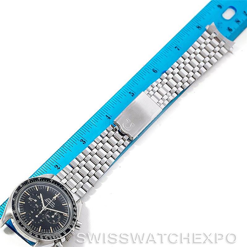 The image shows an Omega Speedmaster Men
s Stainless Steel Black Dial Men
s Stainless Steel Black Dial watch face and partial bracelet laid flat next to a blue ruler.