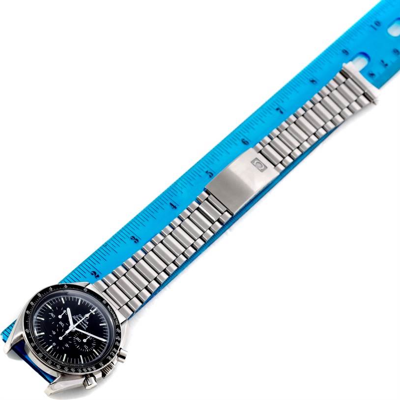 The Omega Speedmaster Men
s Stainless Steel Black Dial Men
s Stainless Steel Black Dial watch is shown flat with its metal bracelet extended next to a blue ruler for scale.