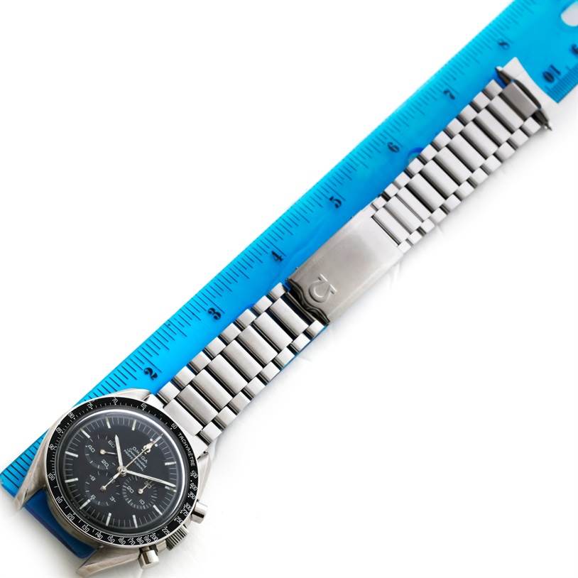 The image displays a top-down view of an Omega Speedmaster Men
s Stainless Steel Black Dial Men
s Stainless Steel Black Dial watch next to a blue ruler.