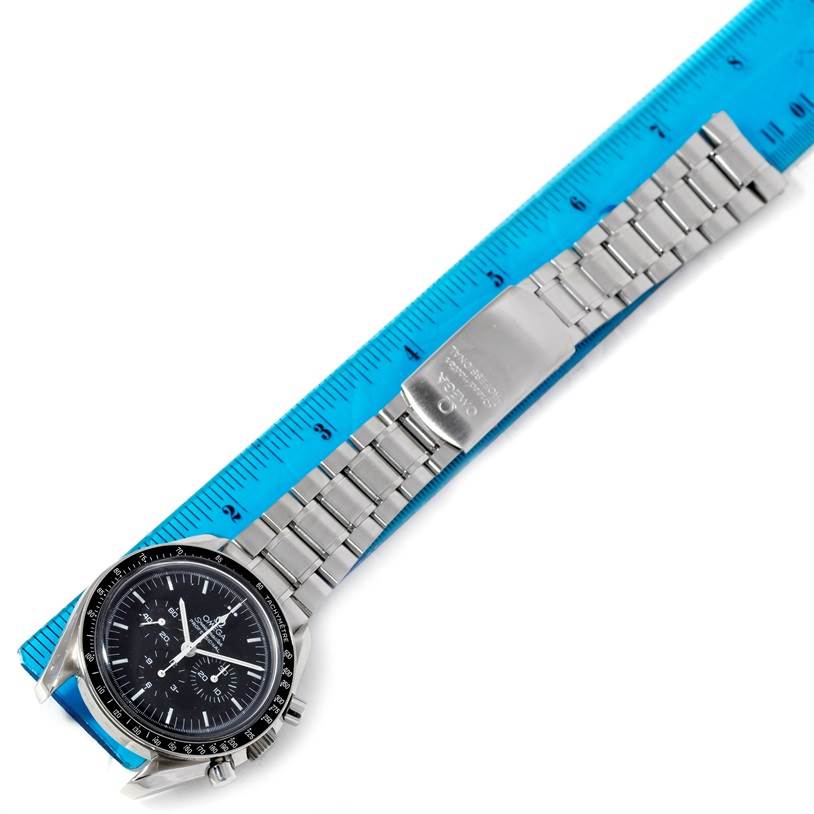 The image shows the Omega Speedmaster 3570.50.00 Men's Stainless Steel Black Dial 3570.50.00 Men's Stainless Steel Black Dial watch laid flat, with a focus on the dial and bracelet against a blue ruler.