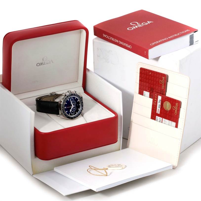 The image shows an Omega Speedmaster 321.33.44.52.01.001 Men
s Stainless Steel Black Dial 321.33.44.52.01.001 Men
s Stainless Steel Black Dial watch in its open box, along with warranty cards, a booklet, and a manual.