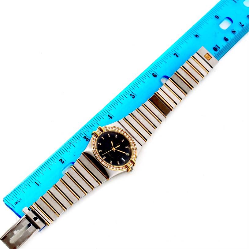 The image shows a top-down view of an Omega Constellation Men's Steel and Gold (two tone) Black Dial Men's Steel and Gold (two tone) Black Dial watch with a blue ruler measuring its length.