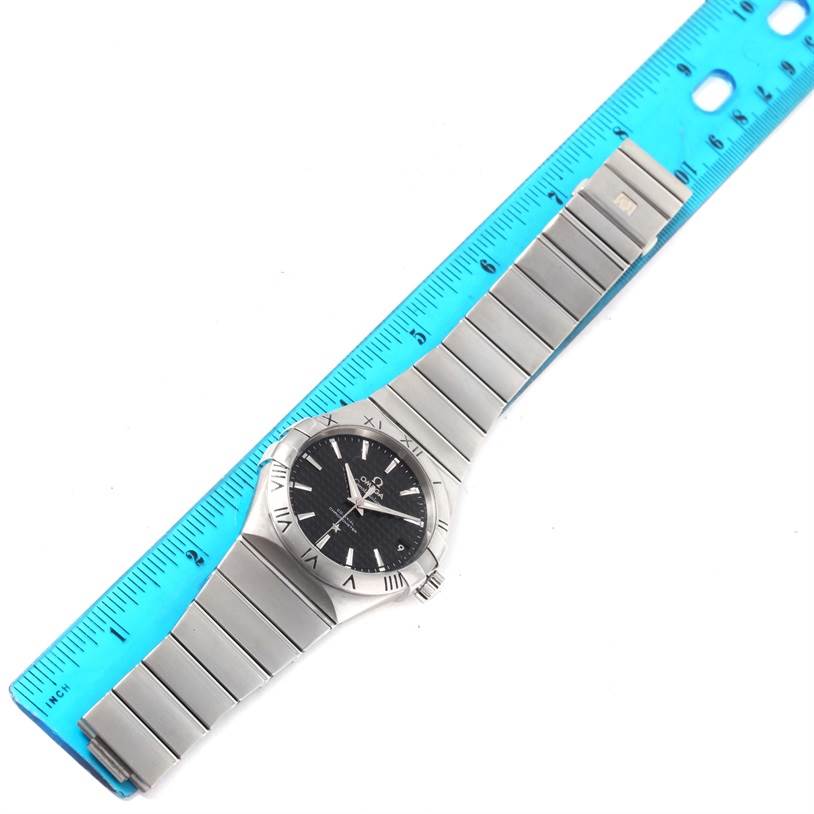 The Omega Constellation 123.10.38.21.01.002 Men's Stainless Steel Black Dial 123.10.38.21.01.002 Men's Stainless Steel Black Dial watch is shown from a top-down angle, displaying the entire band and dial next to a blue ruler.