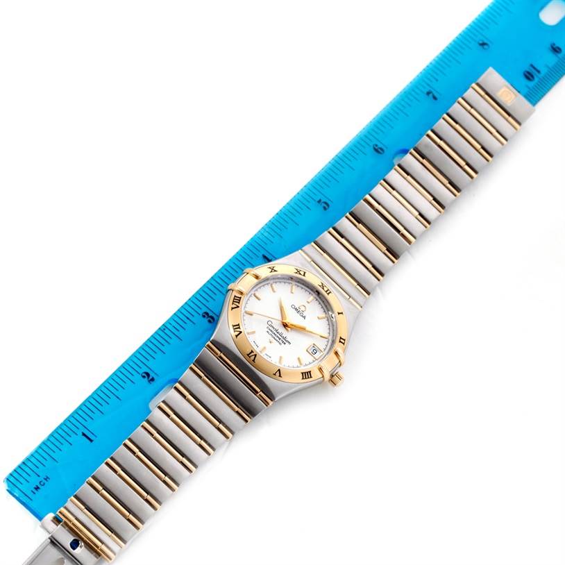 The Omega Constellation 1202.30.00 Men
s Steel and Gold (two tone) Silver Dial 1202.30.00 Men
s Steel and Gold (two tone) Silver Dial watch is shown from a top-down angle, featuring the dial, bezel, and bracelet placed next to a blue ruler.