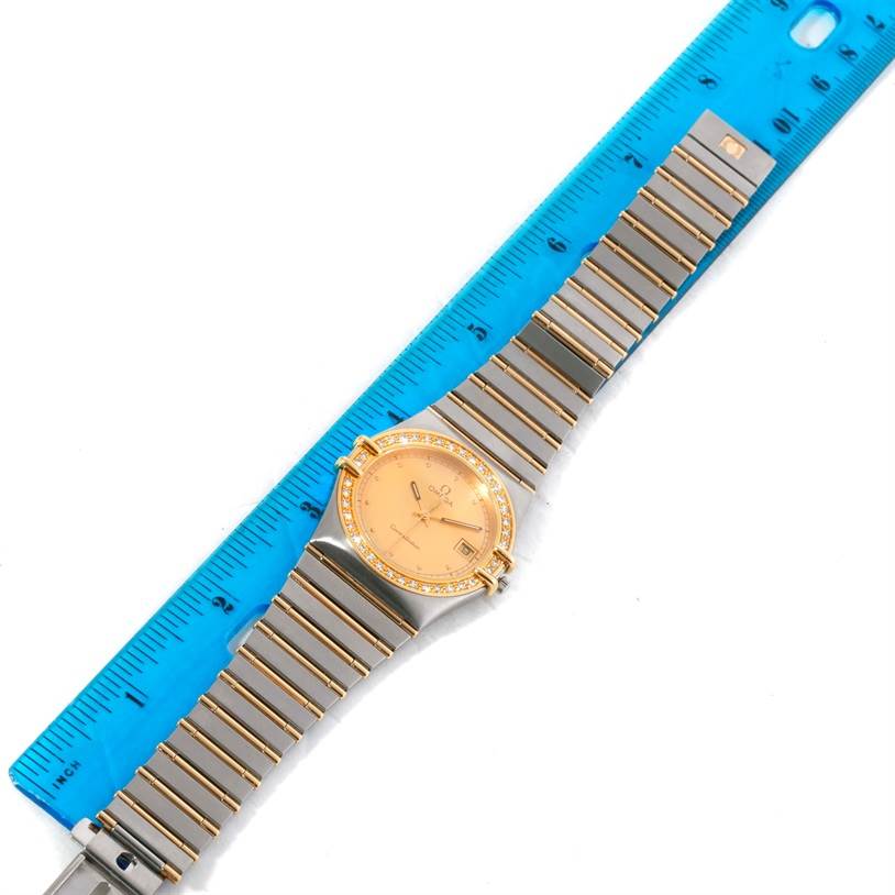 This image shows an Omega Constellation Men's Steel and Gold (two tone) Champagne Dial Men's Steel and Gold (two tone) Champagne Dial watch placed next to a blue ruler for size reference, displaying the face and entire band.