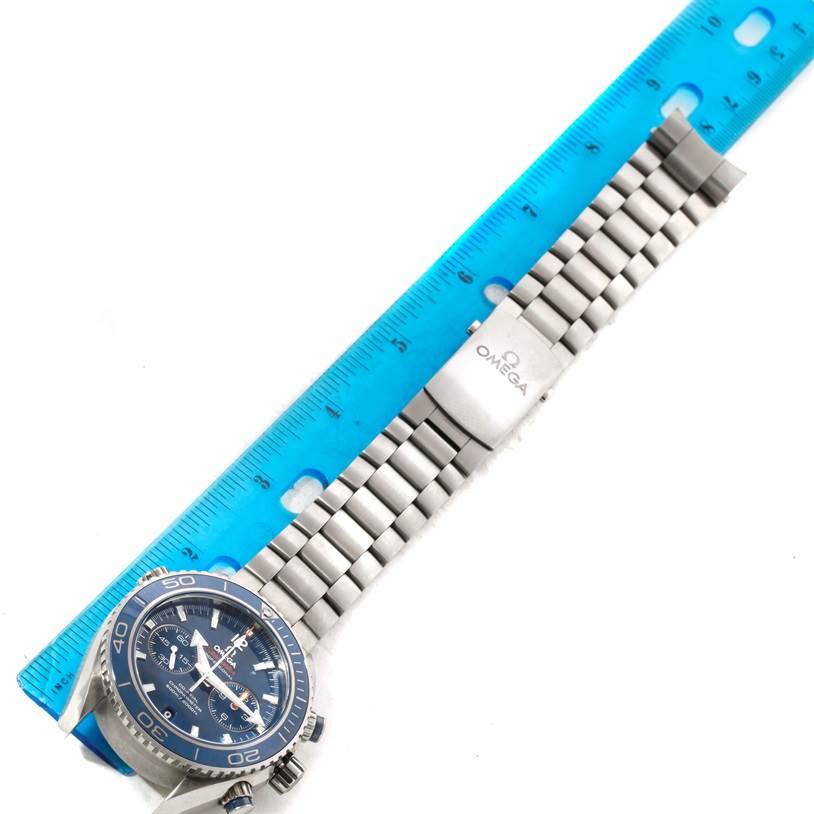 The image shows an Omega Planet Ocean 232.90.46.51.03.001 Men
s Titanium Blue Dial 232.90.46.51.03.001 Men
s Titanium Blue Dial watch laid flat next to a blue ruler, focusing on the face and metal bracelet.