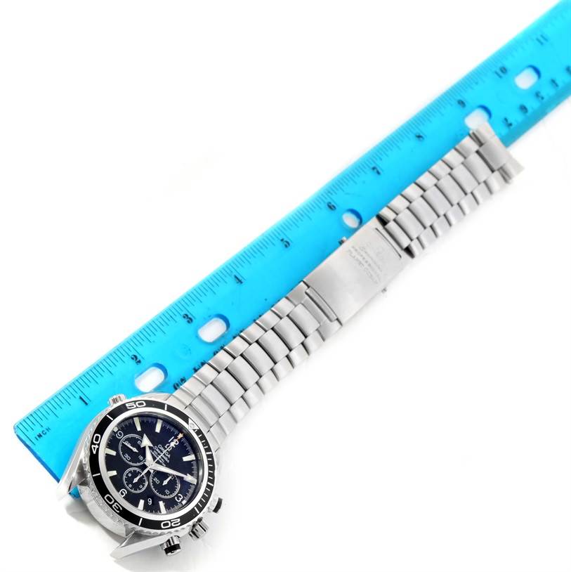 The image shows the Omega Planet Ocean 2210.50.00 Men
s Stainless Steel Black Dial 2210.50.00 Men
s Stainless Steel Black Dial watch positioned diagonally with a blue ruler beside its stainless steel bracelet.