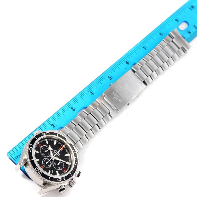 The Omega Planet Ocean 2210.51.00 Men
s Stainless Steel Black Dial 2210.51.00 Men
s Stainless Steel Black Dial watch is shown from a top-down angle, displaying the face, bezel, and metal bracelet next to a blue ruler.