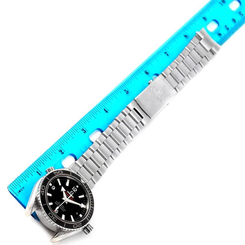 The image shows an Omega Planet Ocean 232.30.42.21.01.001 Men
s Stainless Steel Black Dial 232.30.42.21.01.001 Men
s Stainless Steel Black Dial watch with its stainless steel bracelet next to a blue ruler, viewed from above.