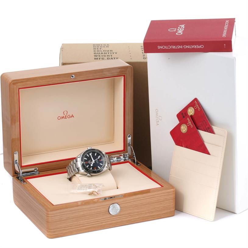 The image shows an Omega Planet Ocean 232.30.46.21.01.003 Men
s Stainless Steel Black Dial 232.30.46.21.01.003 Men
s Stainless Steel Black Dial watch in its open wooden box, along with instruction booklets and warranty cards.