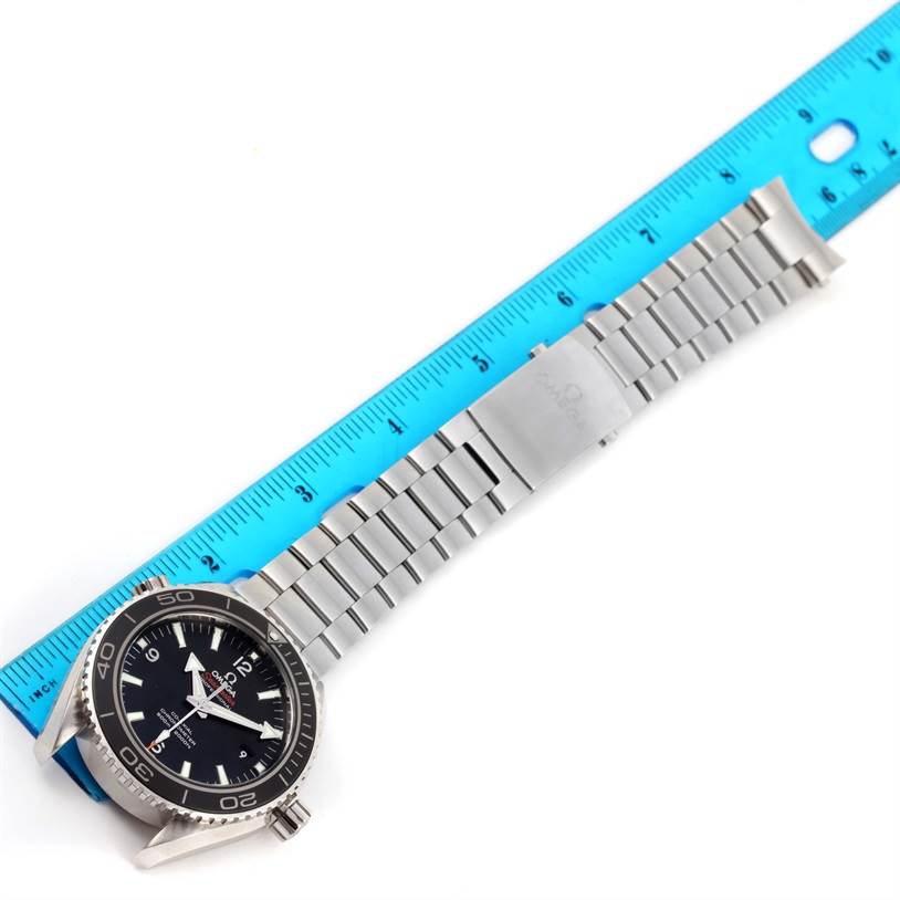 The Omega Planet Ocean 232.30.46.21.01.001 Men
s Stainless Steel Black Dial 232.30.46.21.01.001 Men
s Stainless Steel Black Dial watch is shown from an aerial view, displaying the face, bezel, and metal bracelet next to a blue ruler.