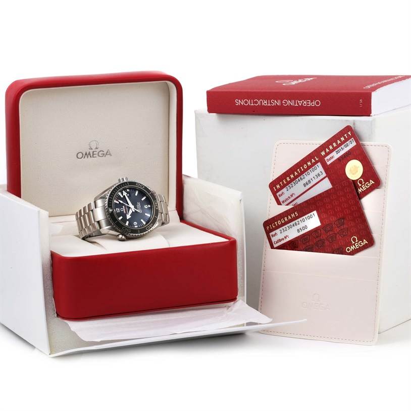 The image shows an Omega Planet Ocean 232.30.46.21.01.001 Men
s Stainless Steel Black Dial 232.30.46.21.01.001 Men
s Stainless Steel Black Dial watch in its open box, alongside an operating instructions book and warranty cards.