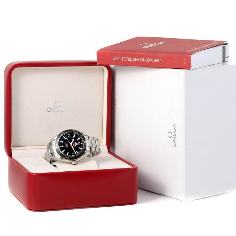 The image shows an Omega Planet Ocean 232.30.42.21.01.001 Men
s Stainless Steel Black Dial 232.30.42.21.01.001 Men
s Stainless Steel Black Dial watch inside a red Omega box with an operating instructions booklet on top of a white box.