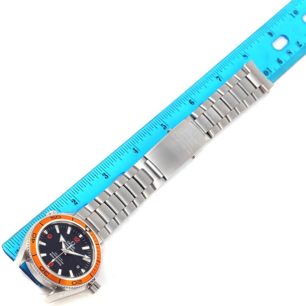 The Omega Planet Ocean 2209.50.00 Men's Stainless Steel Black Dial 2209.50.00 Men's Stainless Steel Black Dial watch is shown laying flat, displaying the face, bezel, bracelet, and clasp next to a blue ruler.