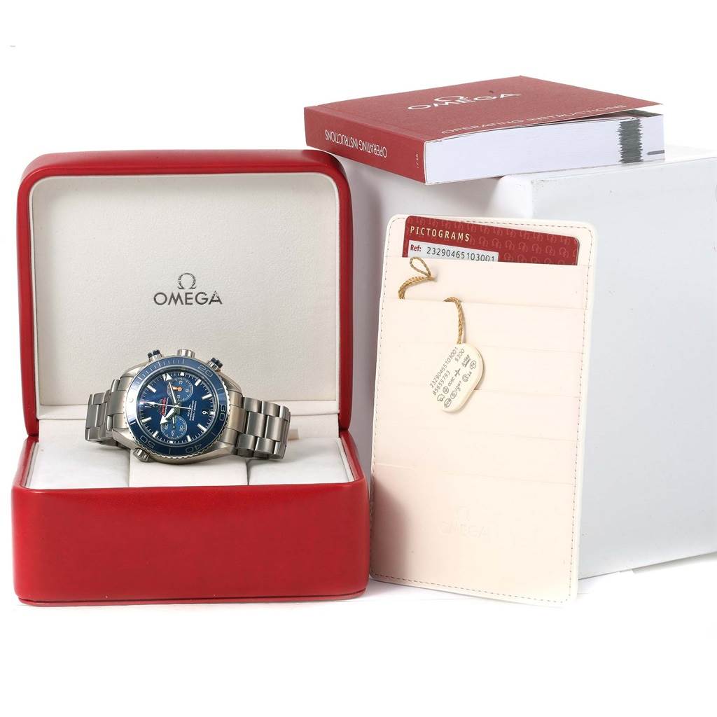 The Omega Planet Ocean 232.90.46.51.03.001 Men's Titanium Blue Dial 232.90.46.51.03.001 Men's Titanium Blue Dial watch is displayed front-facing in its open box, alongside manuals, and certification cards.