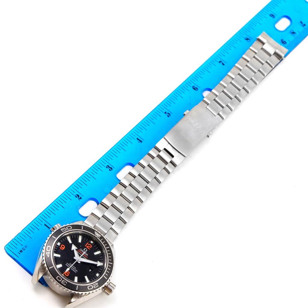 The image shows the front of the Omega Planet Ocean 232.30.38.20.01.002 Men
s Stainless Steel Black Dial 232.30.38.20.01.002 Men
s Stainless Steel Black Dial watch laid next to a ruler, emphasizing the watch
s face and bracelet.