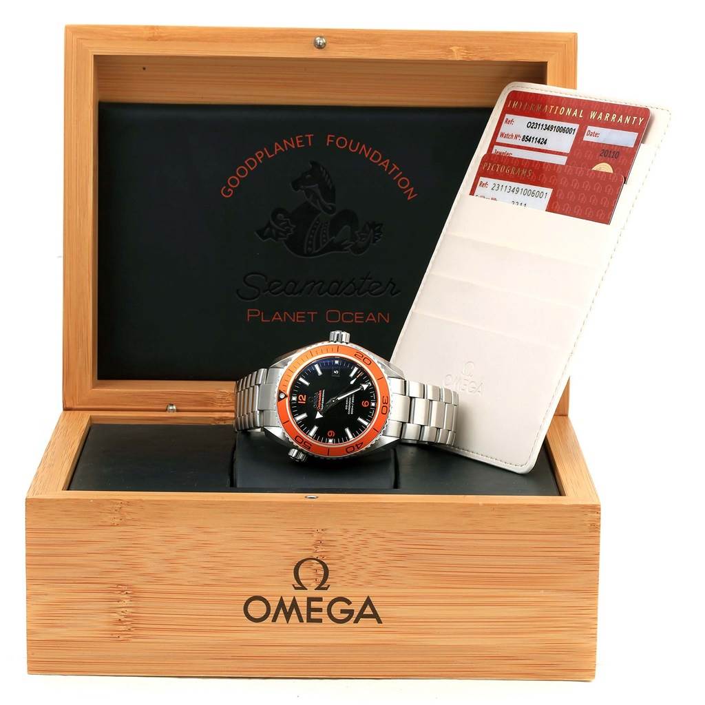 The image shows an Omega Planet Ocean 232.30.46.21.01.002 Men
s Stainless Steel Black Dial 232.30.46.21.01.002 Men
s Stainless Steel Black Dial watch with a metal band, displayed in an open wooden box with a warranty card beside it.