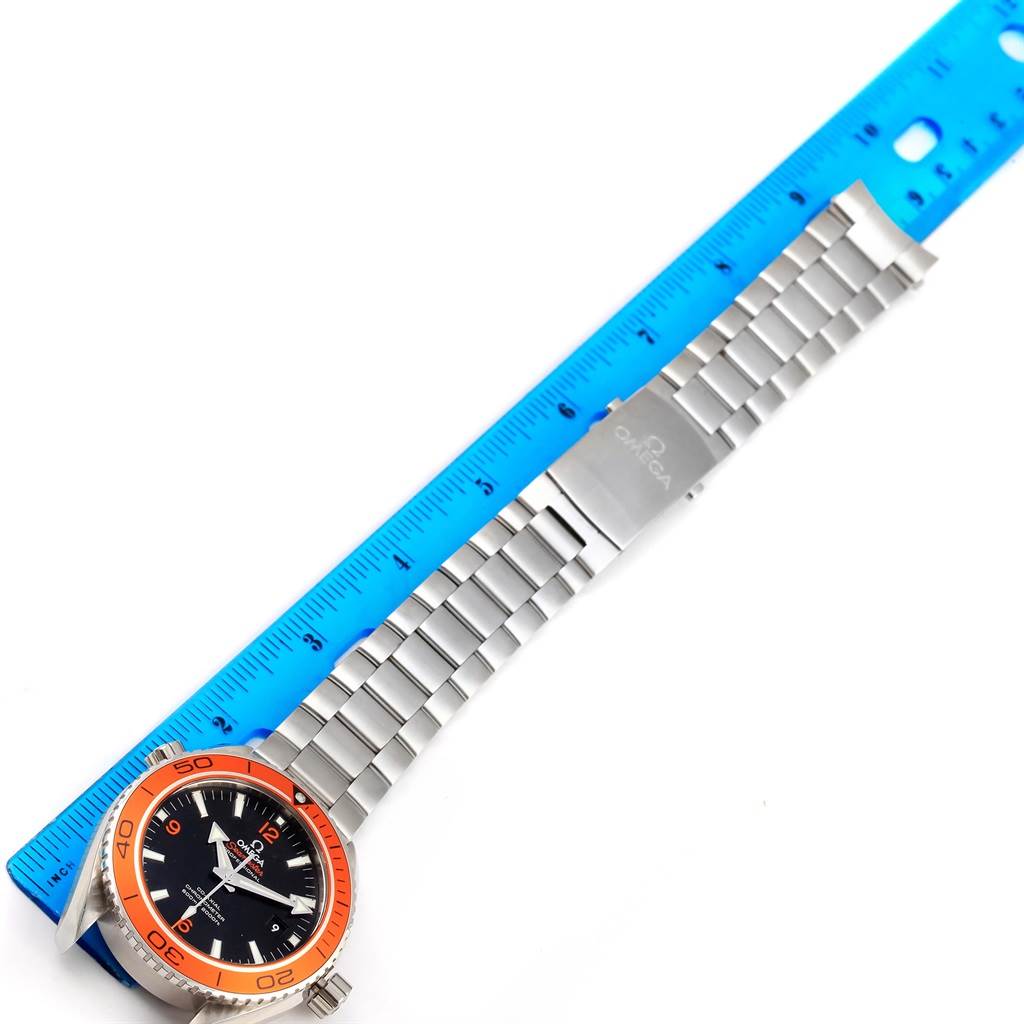 The image shows an Omega Planet Ocean 232.30.46.21.01.002 Men's Stainless Steel Black Dial 232.30.46.21.01.002 Men's Stainless Steel Black Dial watch with an orange bezel, stainless steel bracelet, and clasp, alongside a blue ruler.