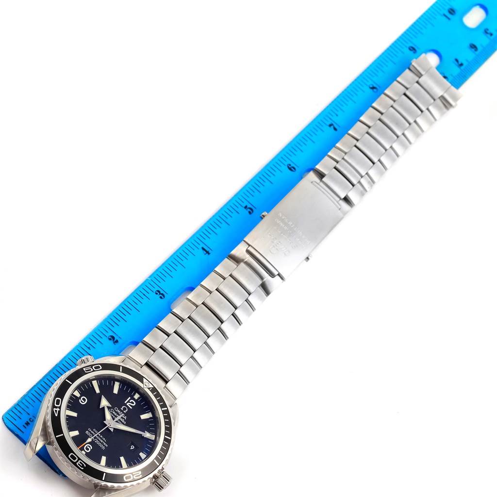 The image shows the Omega Planet Ocean 2200.50.00 Men's Stainless Steel Black Dial 2200.50.00 Men's Stainless Steel Black Dial watch laying flat with its bracelet extended alongside a blue ruler.