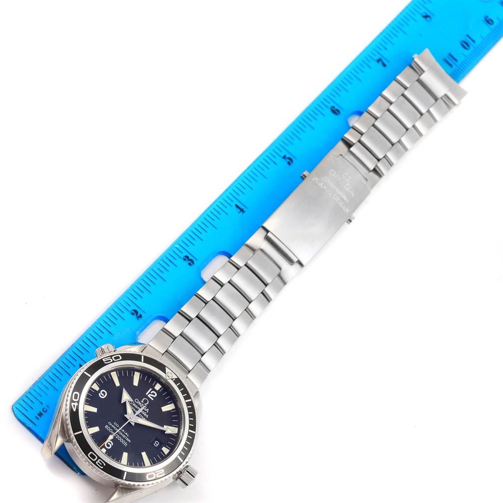 The image shows a top-down view of an Omega Planet Ocean 2201.50.00 Men's Stainless Steel Black Dial 2201.50.00 Men's Stainless Steel Black Dial watch, featuring its face and metal bracelet alongside a blue ruler for scale.