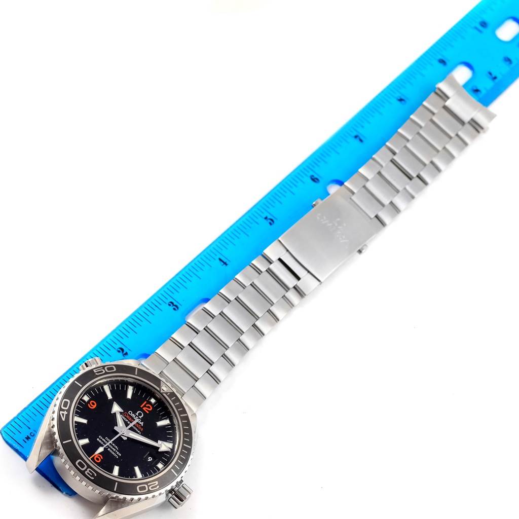 The image shows an overhead view of the Omega Planet Ocean 232.30.46.21.01.003 Men's Stainless Steel Black Dial 232.30.46.21.01.003 Men's Stainless Steel Black Dial watch with its metal strap alongside a blue ruler for scale.