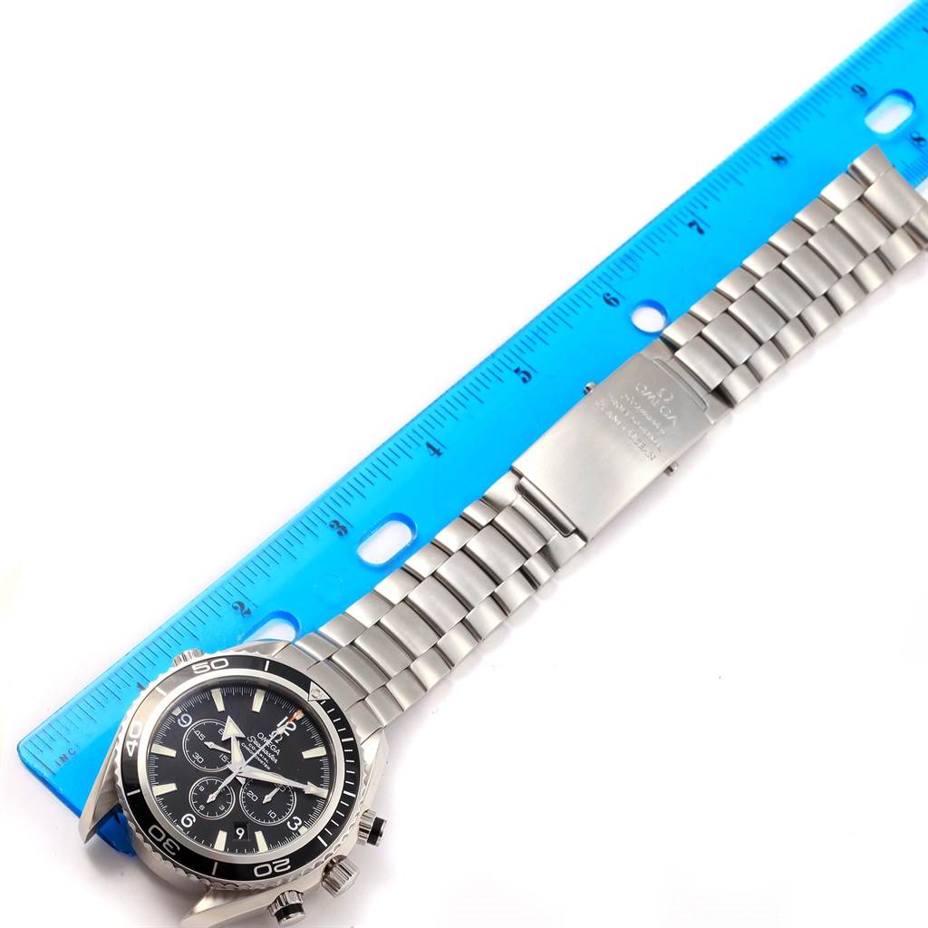 The image shows a top-down view of an Omega Planet Ocean 2210.50.00 Men
s Stainless Steel Black Dial 2210.50.00 Men
s Stainless Steel Black Dial watch, highlighting the face, bezel, and metal bracelet with a blue ruler for scale.