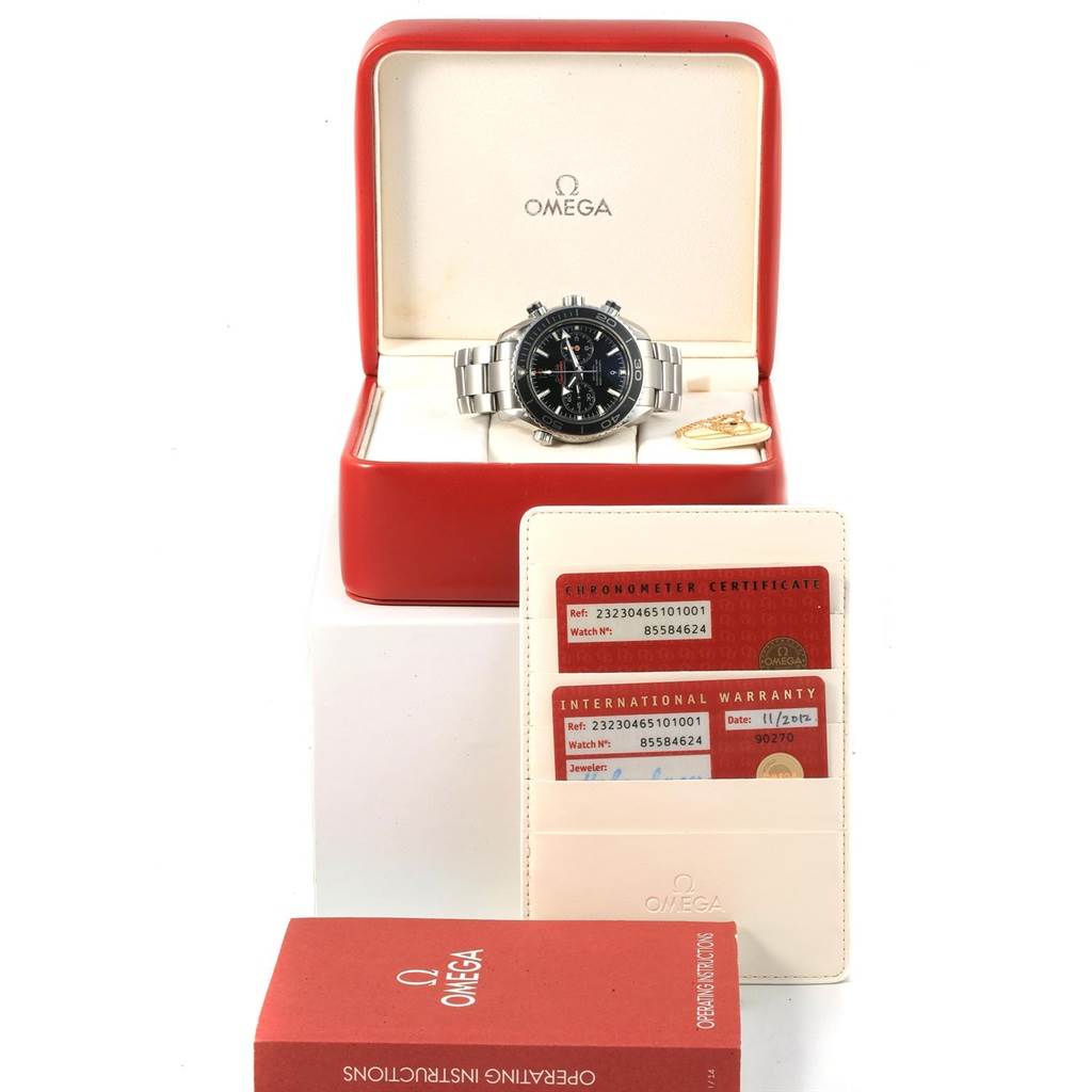 The image shows an Omega Planet Ocean 232.30.46.51.01.001 Men
s Stainless Steel Black Dial 232.30.46.51.01.001 Men
s Stainless Steel Black Dial watch in its box, along with warranty cards and an instruction manual.