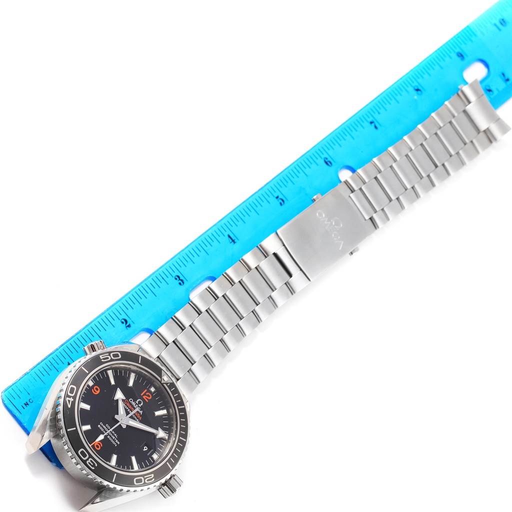 This image shows an Omega Planet Ocean 232.30.46.21.01.003 Men's Stainless Steel Black Dial 232.30.46.21.01.003 Men's Stainless Steel Black Dial watch laid flat with its full metal bracelet and clasp, next to a ruler for scale.