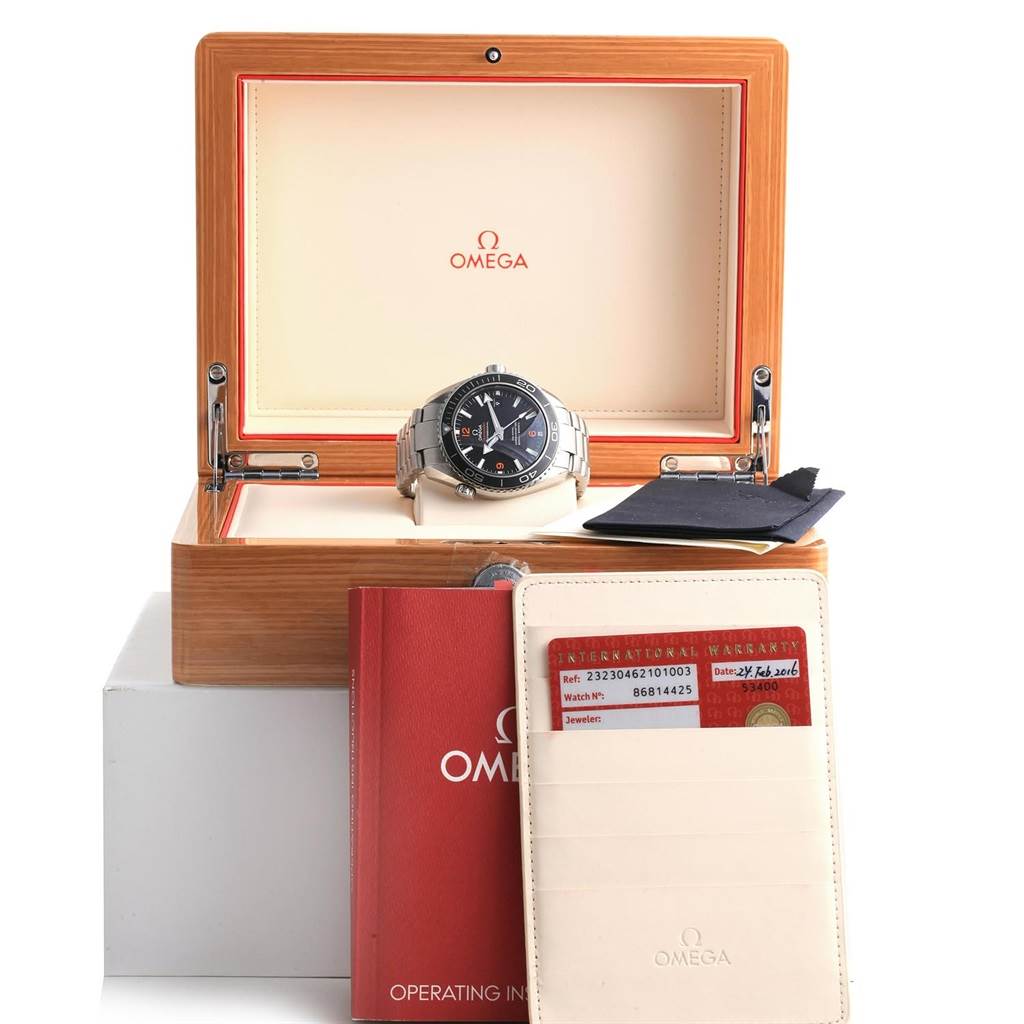 The image shows an Omega Planet Ocean 232.30.46.21.01.003 Men's Stainless Steel Black Dial 232.30.46.21.01.003 Men's Stainless Steel Black Dial watch in an open display box, accompanied by warranty cards and an operating manual.
