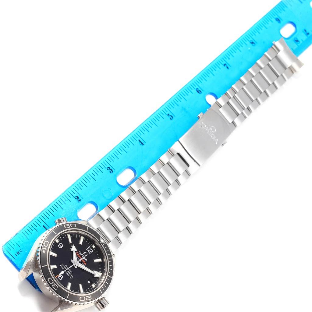 The image shows an Omega Planet Ocean 232.30.42.21.01.001 Men's Stainless Steel Black Dial 232.30.42.21.01.001 Men's Stainless Steel Black Dial watch positioned flat with a blue ruler measuring the length of the metal braceletband.