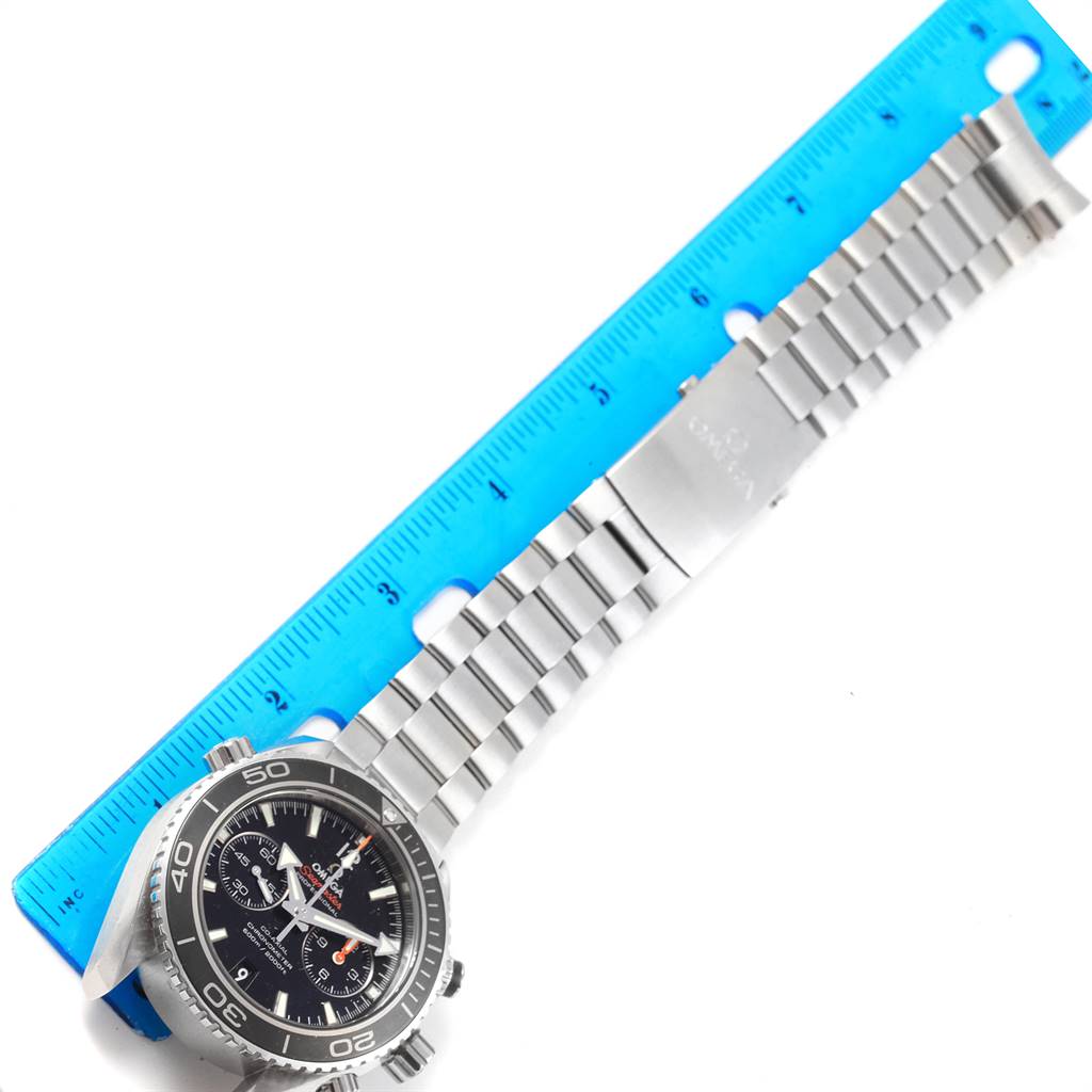 The image shows an Omega Planet Ocean 232.30.46.51.01.001 Men
s Stainless Steel Black Dial 232.30.46.51.01.001 Men
s Stainless Steel Black Dial watch laid flat alongside a blue ruler, displaying the watch face, bezel, and entire metal bracelet.