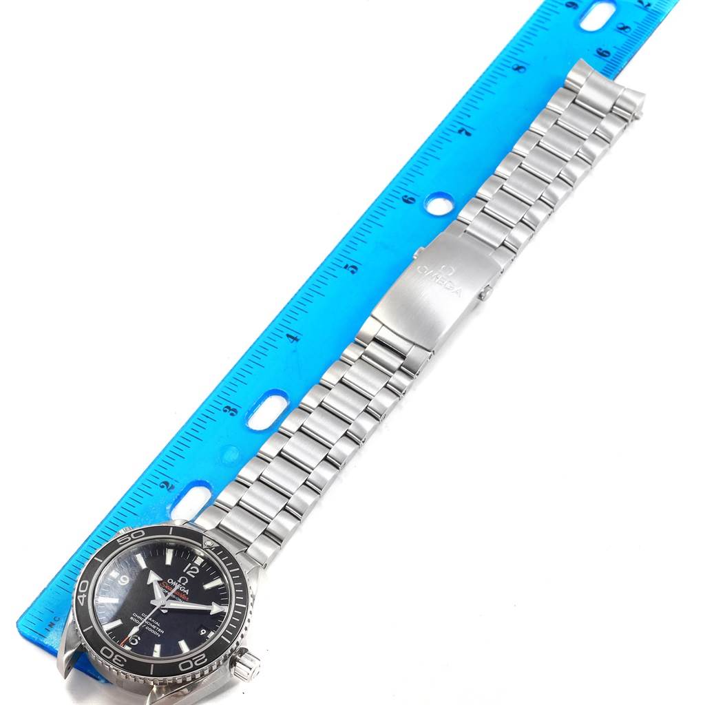 The image shows an Omega Planet Ocean 232.30.42.21.01.001 Men's Stainless Steel Black Dial 232.30.42.21.01.001 Men's Stainless Steel Black Dial watch, viewed from above, with a stainless steel bracelet and clasp, alongside a blue ruler.