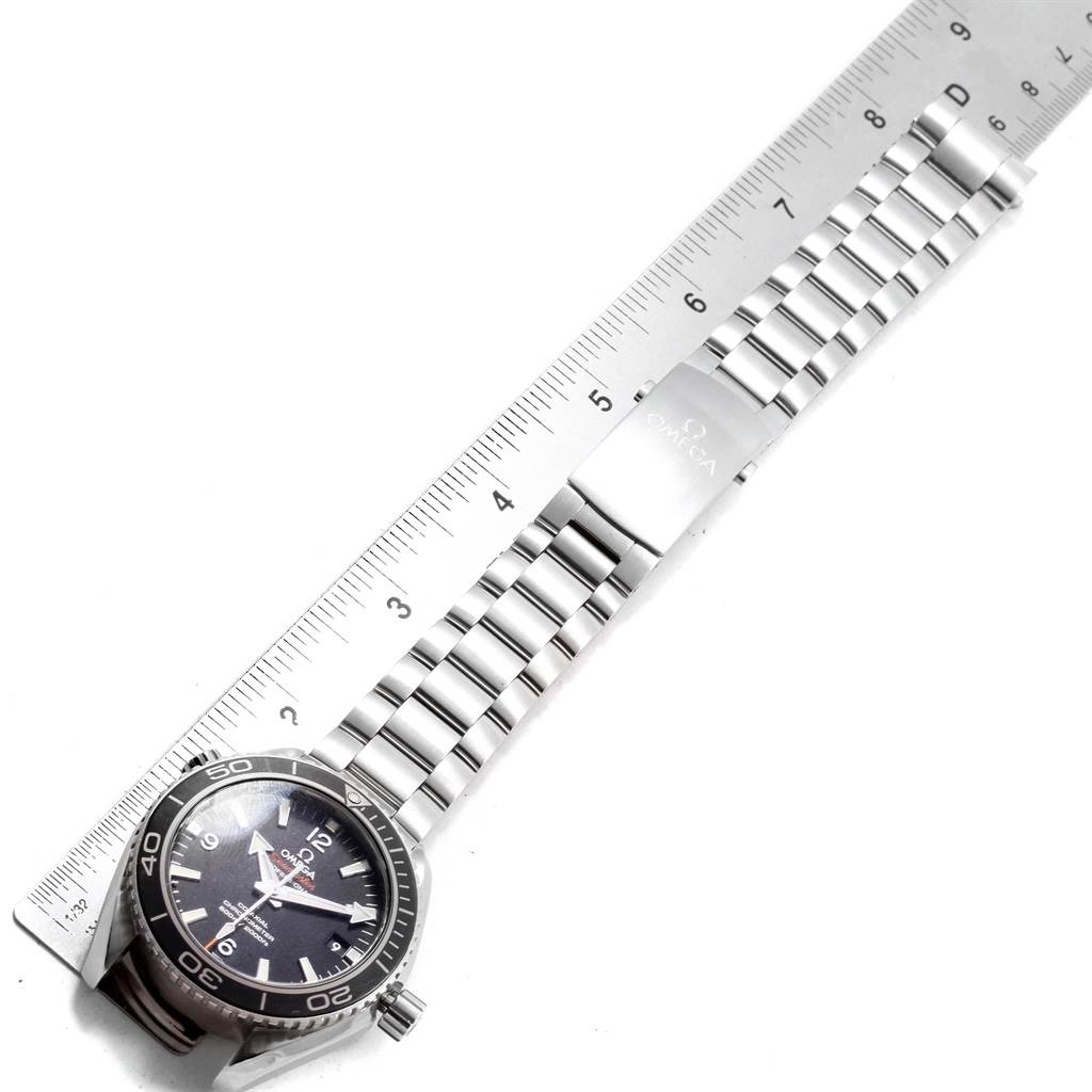 The image shows an Omega Planet Ocean 232.30.42.21.01.001 Men
s Stainless Steel Black Dial 232.30.42.21.01.001 Men
s Stainless Steel Black Dial watch model, showcasing its bezel, face, and metal strap beside a measuring ruler.