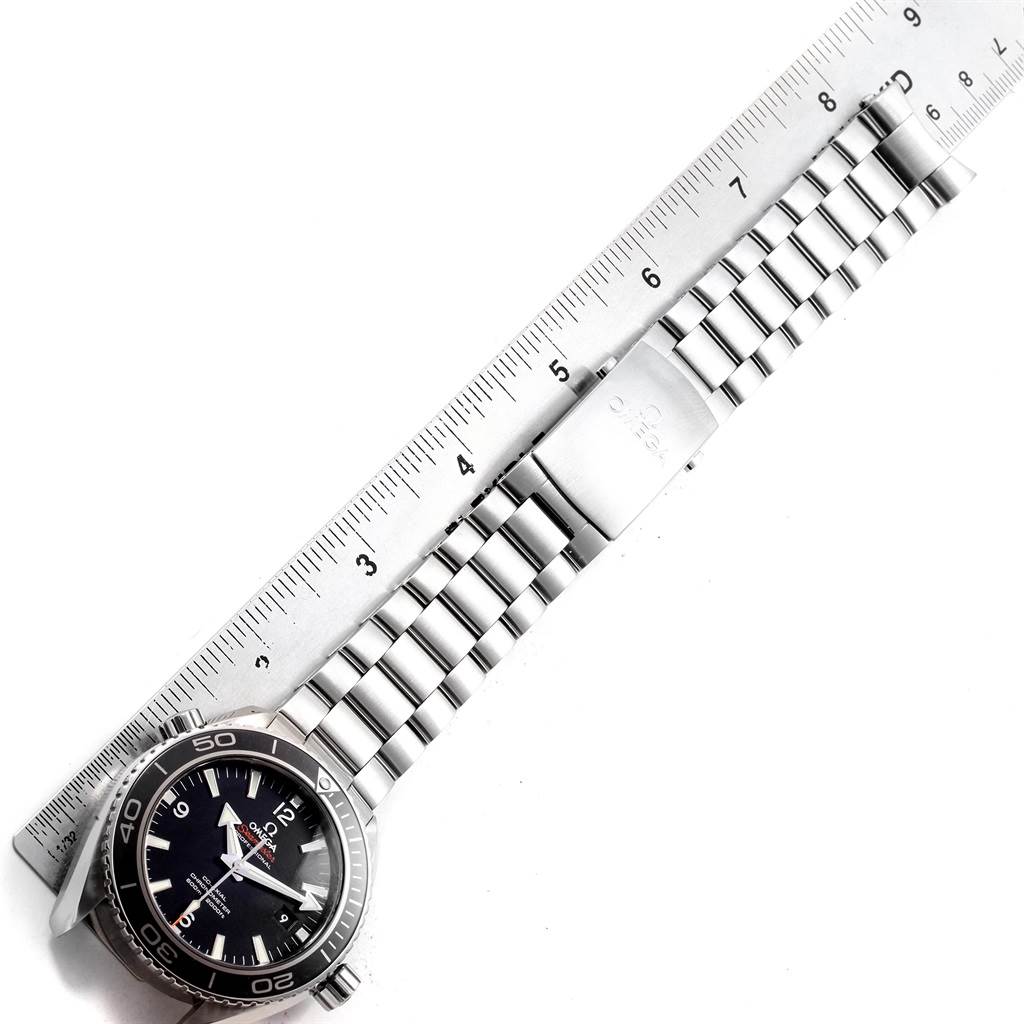 The photo shows an Omega Planet Ocean 232.30.46.21.01.001 Men
s Stainless Steel Black Dial 232.30.46.21.01.001 Men
s Stainless Steel Black Dial watch with its bracelet and clasp in a top-down angle, laid next to a ruler.