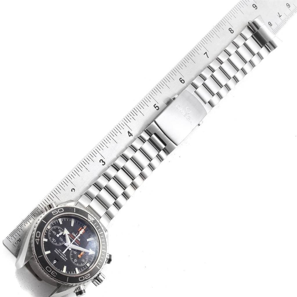 The image shows an Omega Planet Ocean 232.30.46.51.01.003 Men's Stainless Steel Black Dial 232.30.46.51.01.003 Men's Stainless Steel Black Dial watch laid flat, with a ruler indicating the length of its stainless steel bracelet.