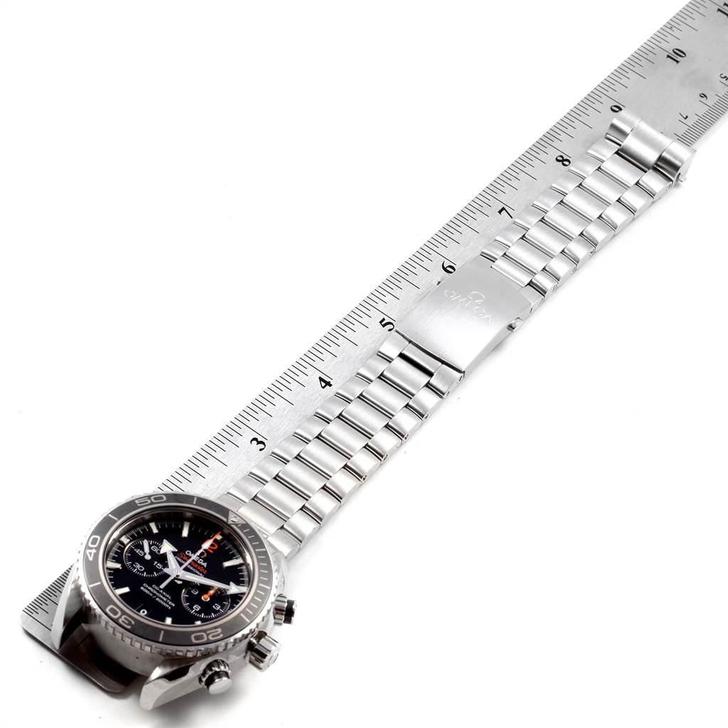 The image shows the Omega Planet Ocean 232.30.42.21.01.003 Men
s Stainless Steel Black Dial 232.30.42.21.01.003 Men
s Stainless Steel Black Dial watch laid flat with its face, bezel, bracelet, and clasp visible beside a measuring ruler.