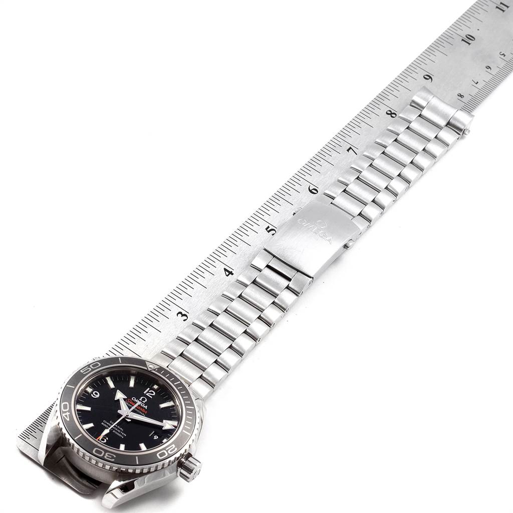 The image shows an Omega Planet Ocean 232.30.46.21.01.001 Men
s Stainless Steel Black Dial 232.30.46.21.01.001 Men
s Stainless Steel Black Dial watch laid flat alongside a ruler, highlighting the bezel, face, and metal bracelet.