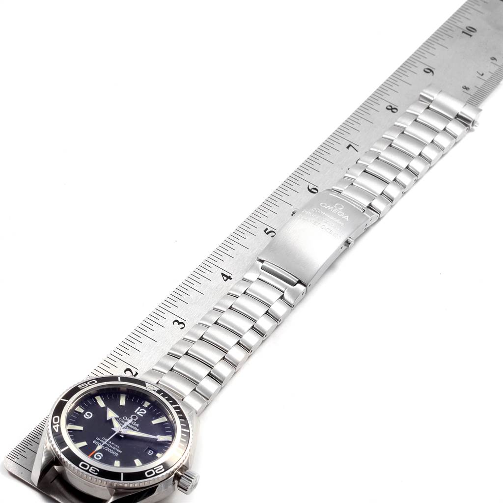 This image shows an Omega Planet Ocean 2201.50.00 Men
s Stainless Steel Black Dial 2201.50.00 Men
s Stainless Steel Black Dial watch laid flat alongside a metal ruler, displaying its face and full metal bracelet.