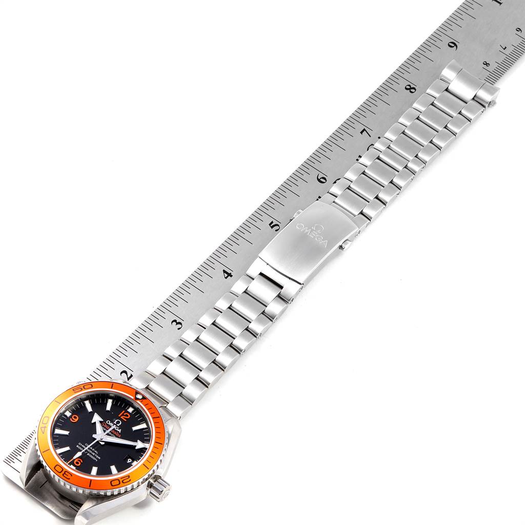 The image shows an Omega Planet Ocean 232.30.42.21.01.002 Men
s Stainless Steel Black Dial 232.30.42.21.01.002 Men
s Stainless Steel Black Dial watch laid flat with a ruler, highlighting its stainless steel bracelet and orange bezel.