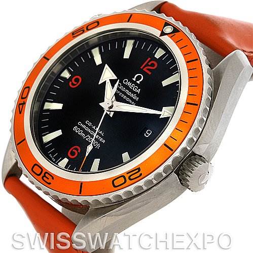 The image shows an angled view of the Omega Planet Ocean 2908.50.83 Men's Stainless Steel Black Dial 2908.50.83 Men's Stainless Steel Black Dial watch face, bezel, and crown, featuring an orange bezel and red strap.