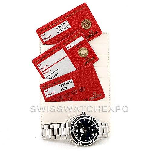 The image shows an Omega Planet Ocean 2200.50.00 Men
s Stainless Steel Black Dial 2200.50.00 Men
s Stainless Steel Black Dial watch with its metal bracelet and warranty cards, laid flat from a top-down angle.