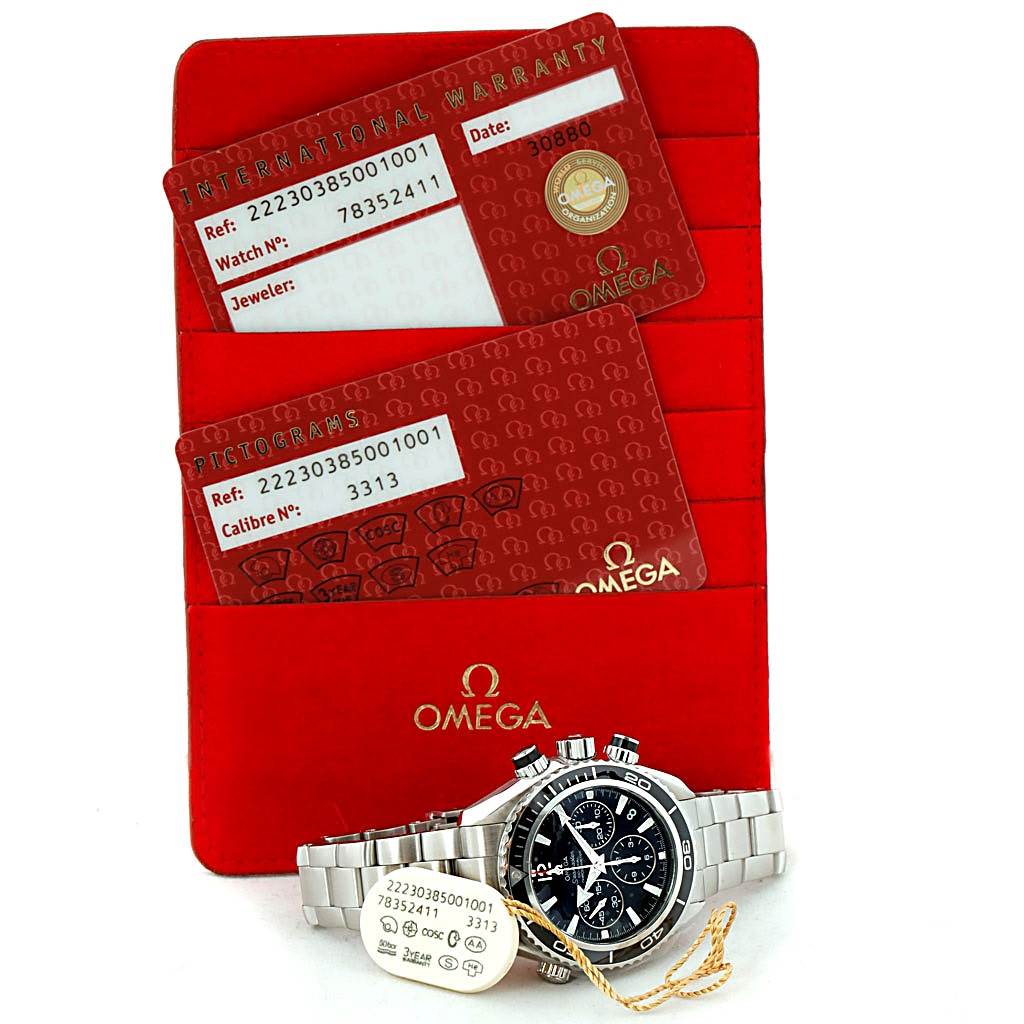 The Omega Planet Ocean 222.30.38.50.01.001 Stainless Steel Black Dial 222.30.38.50.01.001 Stainless Steel Black Dial watch is shown front-facing with its warranty cards and red cardholder behind it.