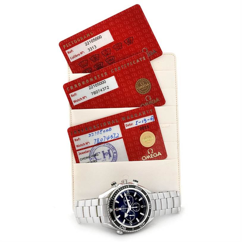 The image shows an Omega Planet Ocean 2210.50.00 Men
s Stainless Steel Black Dial 2210.50.00 Men
s Stainless Steel Black Dial watch with a metal strap, placed in front of its certification and warranty cards.