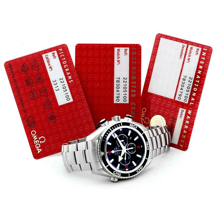 The image shows an Omega Planet Ocean 2210.51.00 Men's Stainless Steel Black Dial 2210.51.00 Men's Stainless Steel Black Dial watch laying flat with its face and bracelet visible, along with three red warranty and info cards.