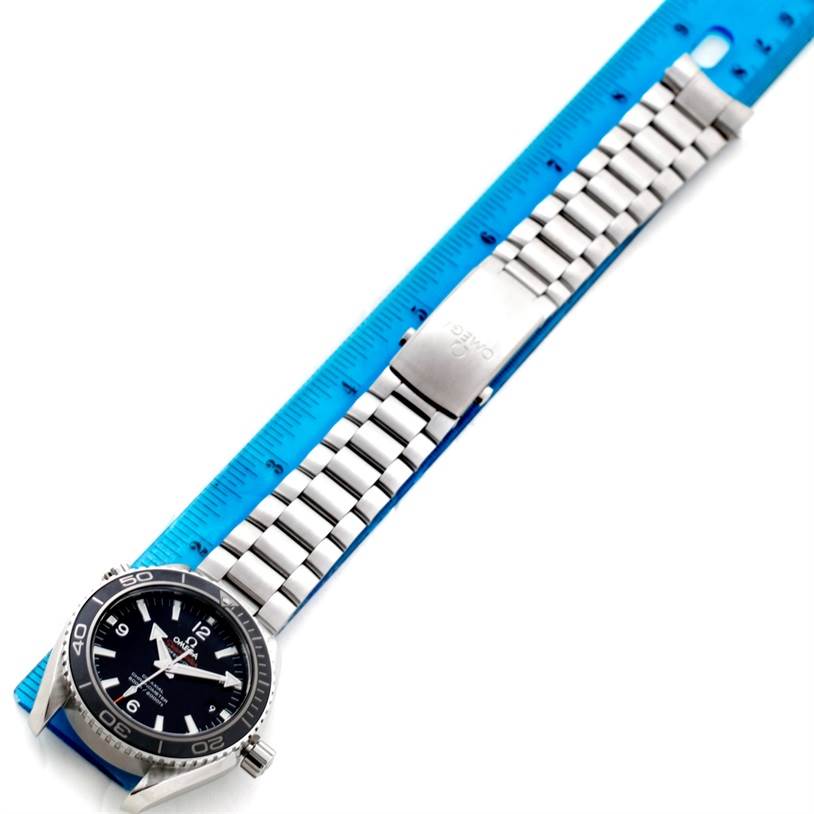 The Omega Planet Ocean 232.30.42.21.01.003 Men's Stainless Steel Black Dial 232.30.42.21.01.003 Men's Stainless Steel Black Dial watch is shown from a top-down angle, highlighting the face, bezel, and metal bracelet against a blue ruler.