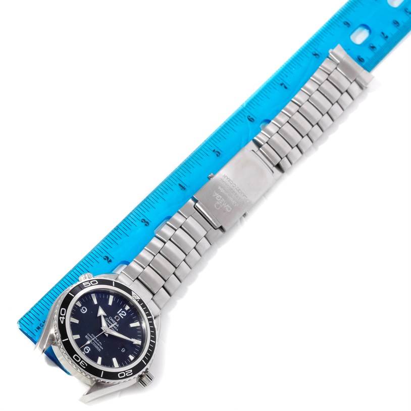 The image shows the Omega Planet Ocean 2200.50.00 Men's Stainless Steel Black Dial 2200.50.00 Men's Stainless Steel Black Dial watch laid flat with its stainless steel bracelet fully extended next to a blue ruler.